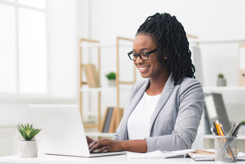 A professional woman in a business suit happily typing on her laptop, focused on her work.