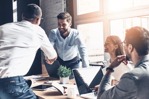 A diverse group of individuals shaking hands at a table, symbolizing collaboration and partnership.