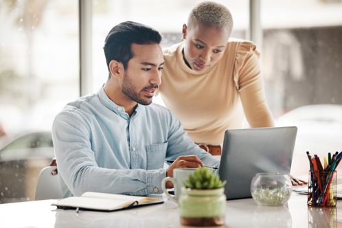 A man and woman collaborating on a laptop, engaged in productive work together.