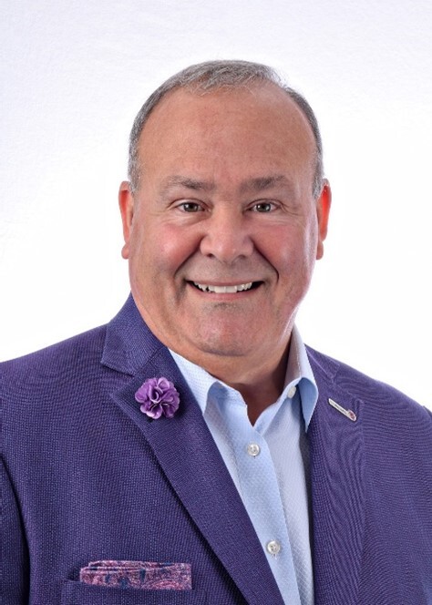 A man in a purple suit and tie, wearing a smile on his face.
